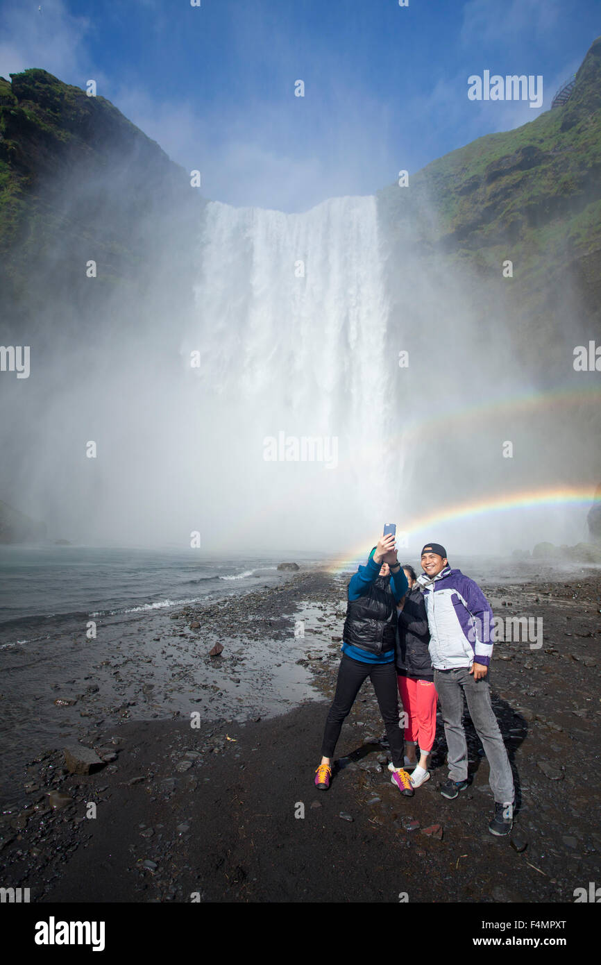 Touristen in den Regenbogen unter 60m hohen Skogafoss Wasserfall, Skogar, Sudhurland, Island. Stockfoto