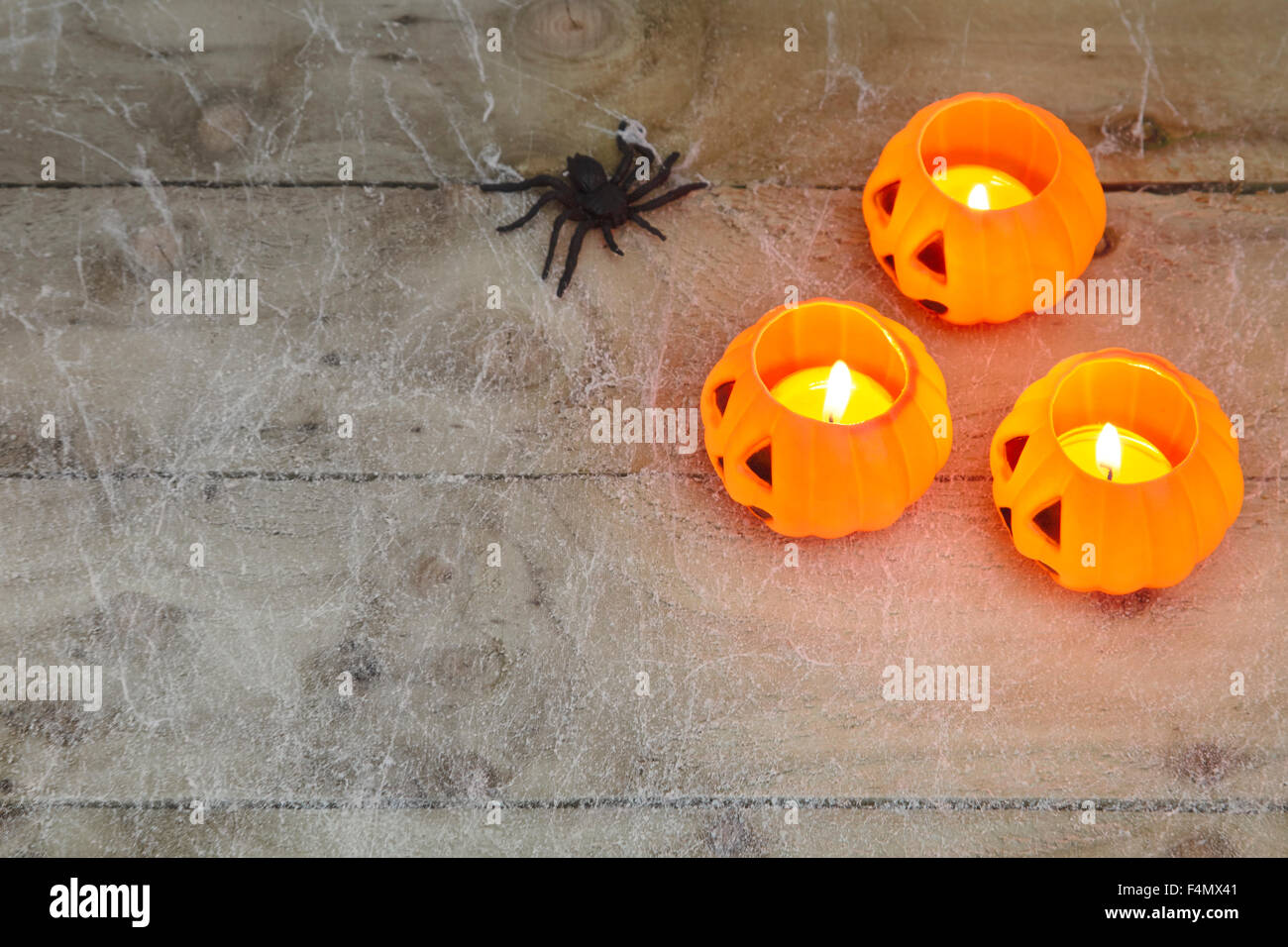 Halloween-Konzept mit einem orange glühenden Kürbis Form Teelicht Kerzenhalter und Spielzeug Spinne auf einem dunklen Spinnennetz-Hintergrund Stockfoto