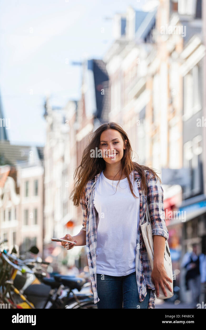 Niederlande, Amsterdam, lächelnde junge Frau in der Stadt mit Handy Stockfoto