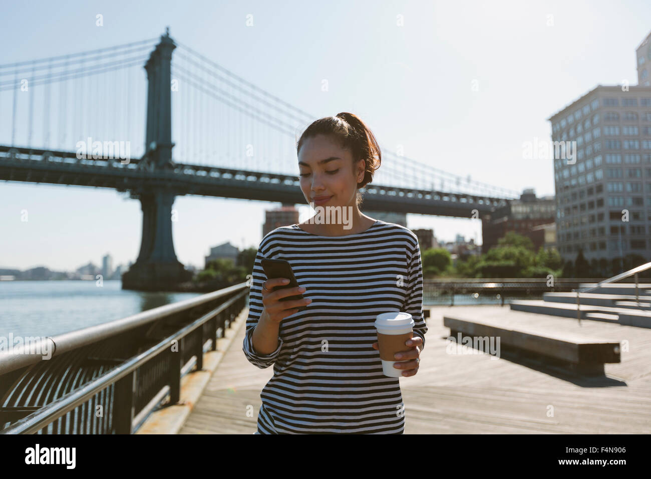 USA, New York City, Porträt der lächelnde junge Frau mit Kaffee auf ihrem Smartphone suchen Stockfoto