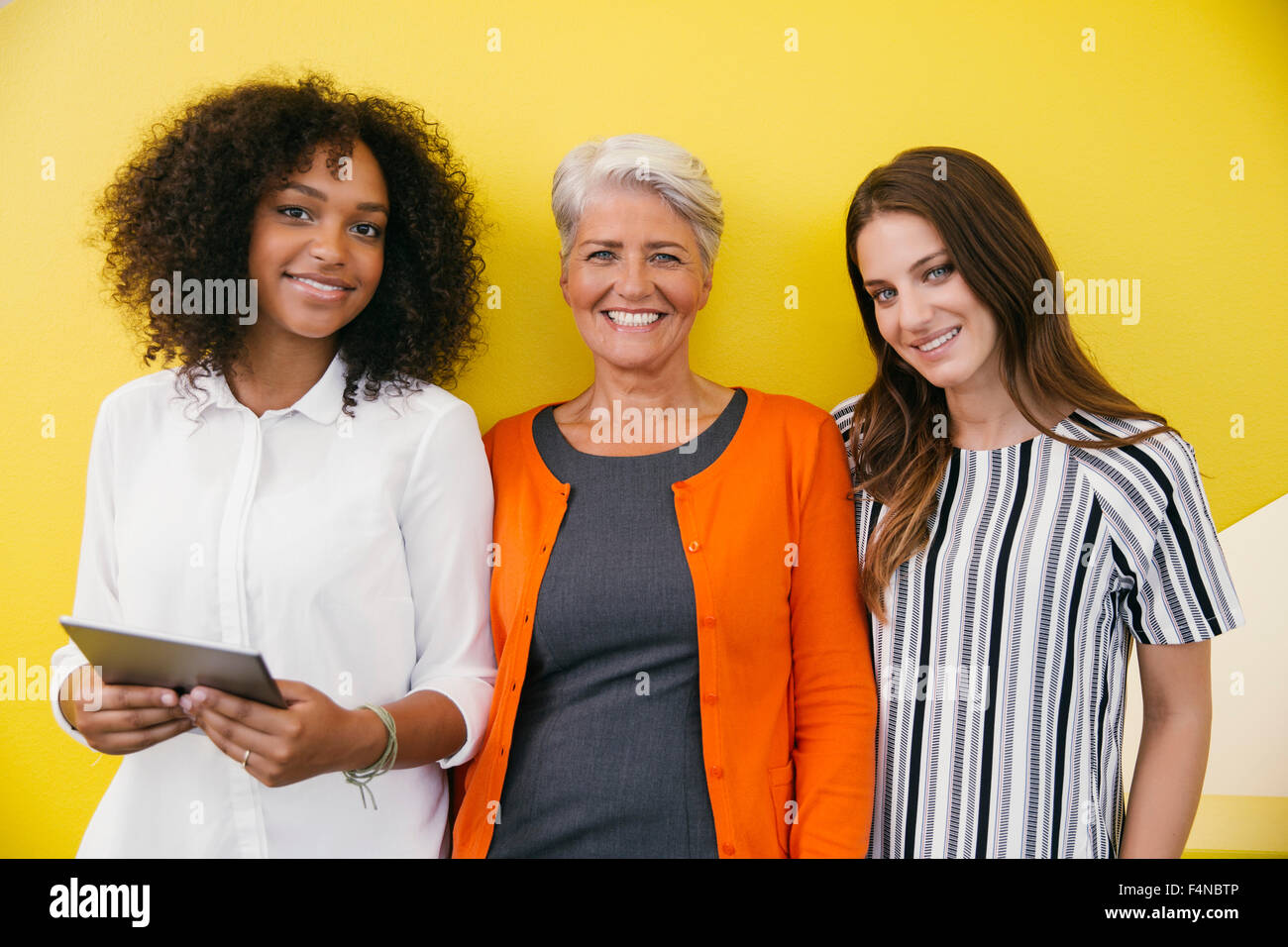 Gruppenbild der drei lächelnde Frauen stehen vor einer gelben Wand Stockfoto