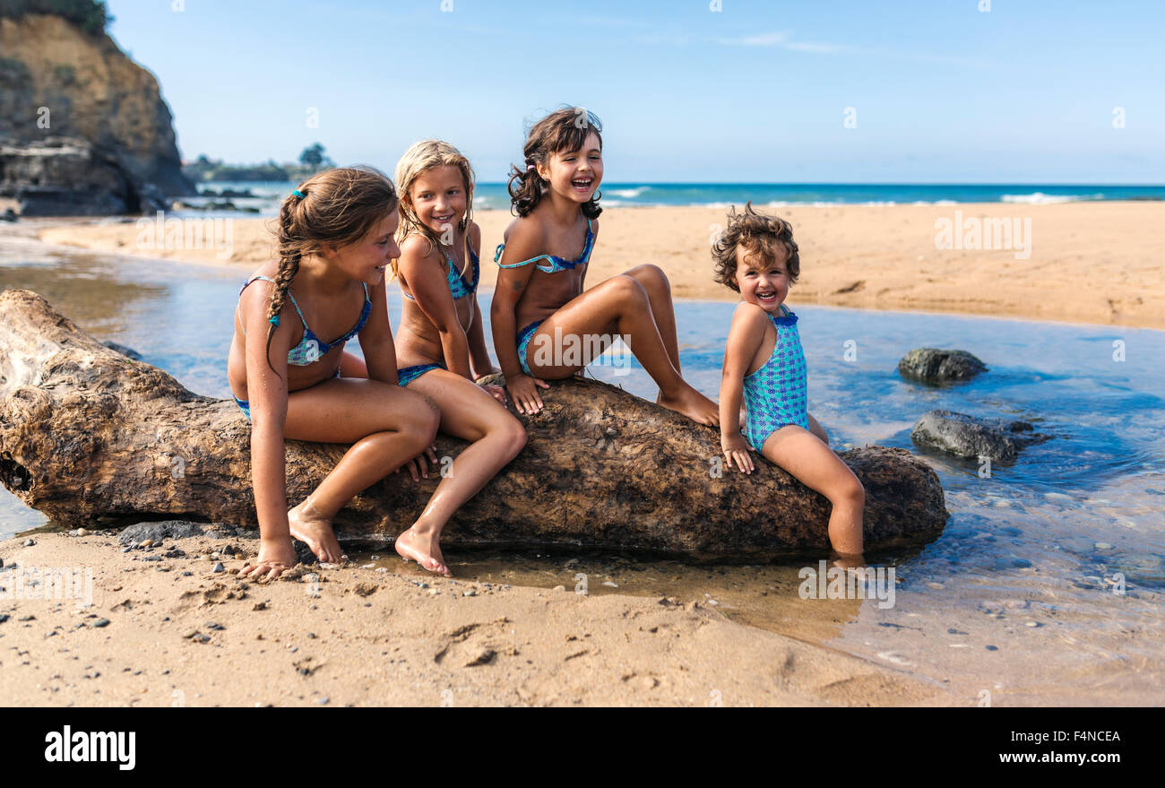 Spanien, Colunga, vier Mädchen sitzen auf abgestorbenem Holz am Strand Stockfoto