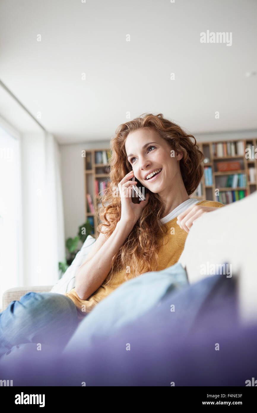 Lächelnde Frau zu Hause sitzen auf Couch reden über Handy Stockfoto