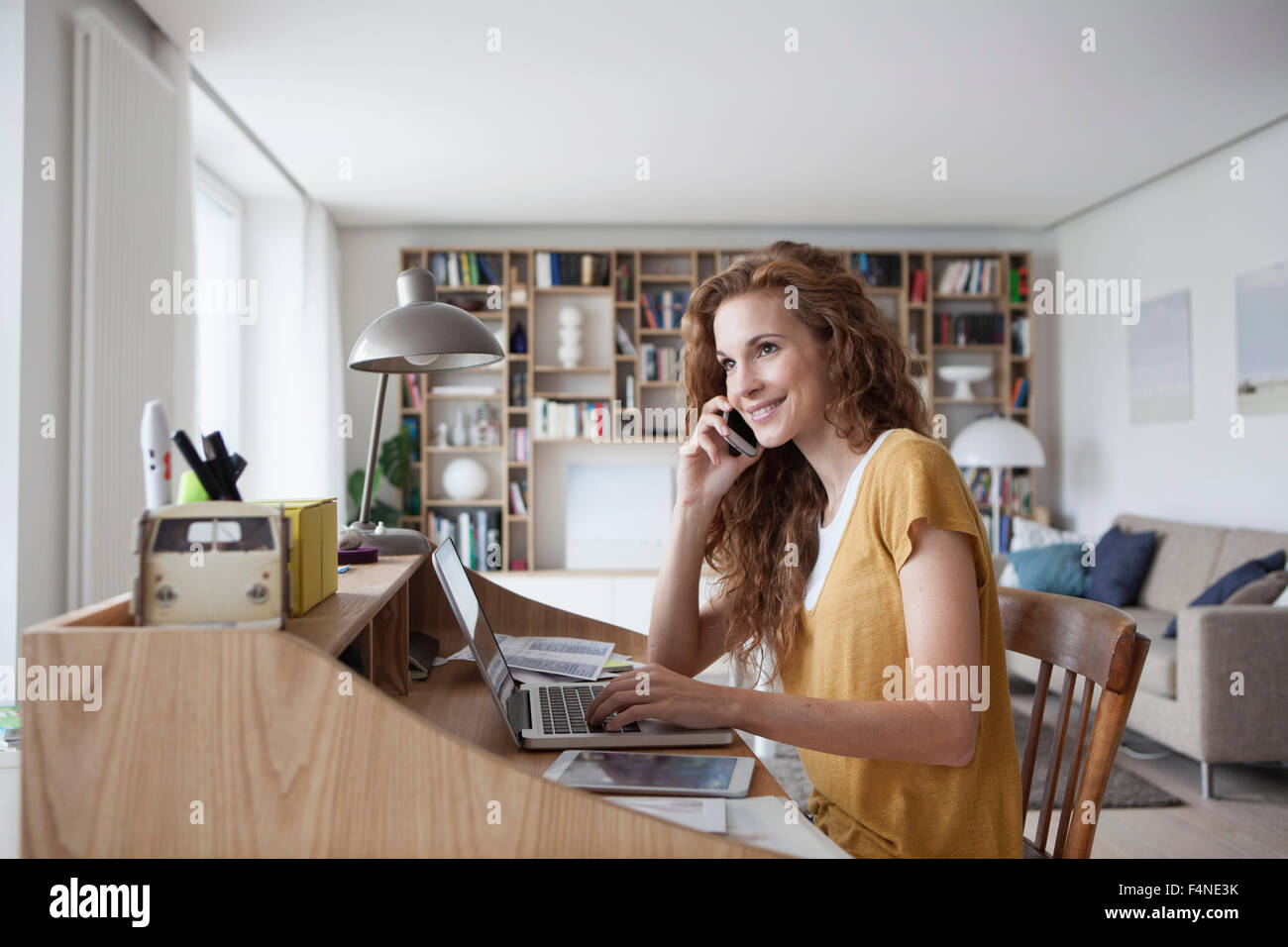 Lächelnde Frau mit Handy, digitale Tablet und Laptop auf Sekretär Schreibtisch zu Hause Stockfoto