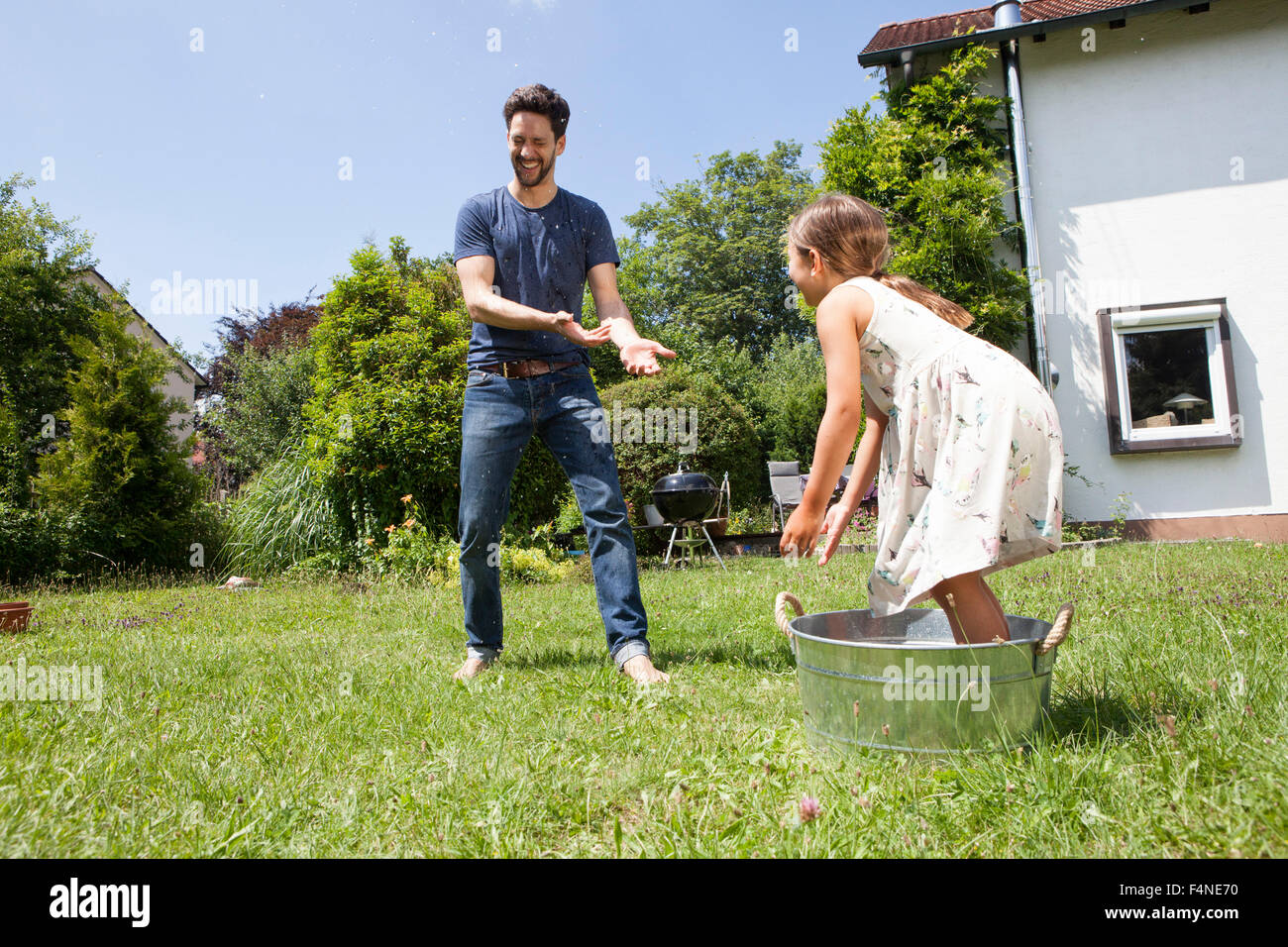 Vater und Tochter, spritzt mit Wasser im Garten Stockfoto