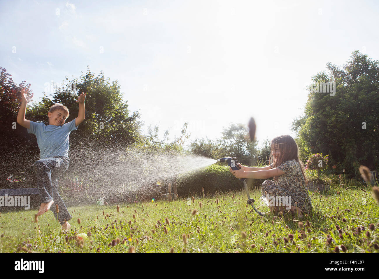 Jungen und Mädchen Spritzen mit Wasser im Garten Stockfoto