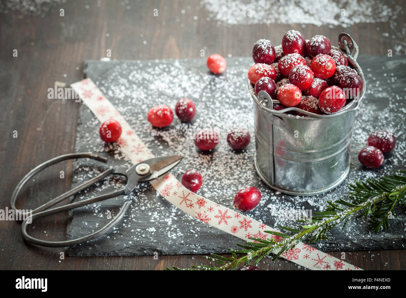 Cranberries in kleine Zink Eimer, Vereisung, Schere und Farbband auf Schiefer, Holz Stockfoto