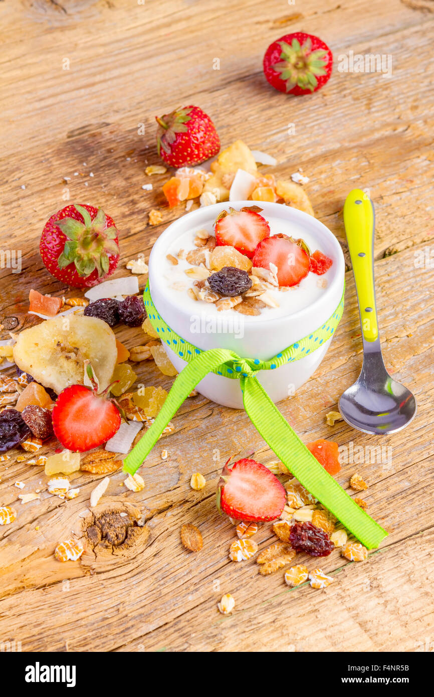 Joghurt mit Müsli Müsli, frische Erdbeeren, Banane und Rosinen in Schüssel auf hölzernen Hintergrund Stockfoto