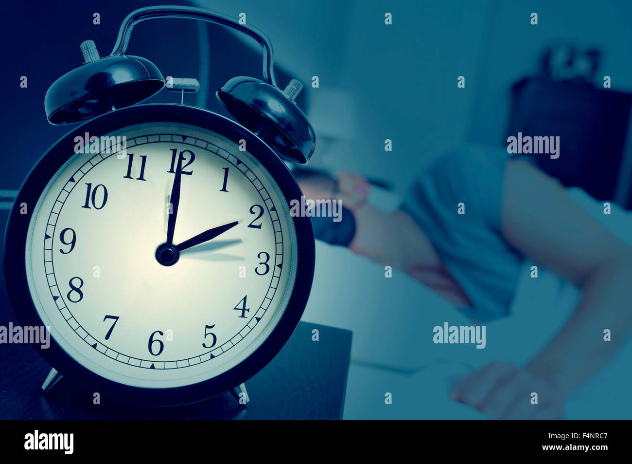 Nahaufnahme eines Weckers auf einem Nachttisch rückwärts eine Stunde am Ende der Sommerzeit anpassen, während ein junger Mann in schläft Stockfoto