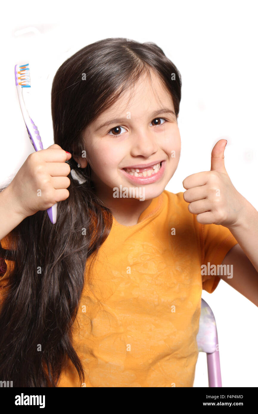 Sieben Jahres altes Mädchen zeigt großes Lächeln zeigt, fehlen die oberen Schneidezähne und halten eine Zahnbürste und Daumen nach oben auf eine weiße bac Stockfoto