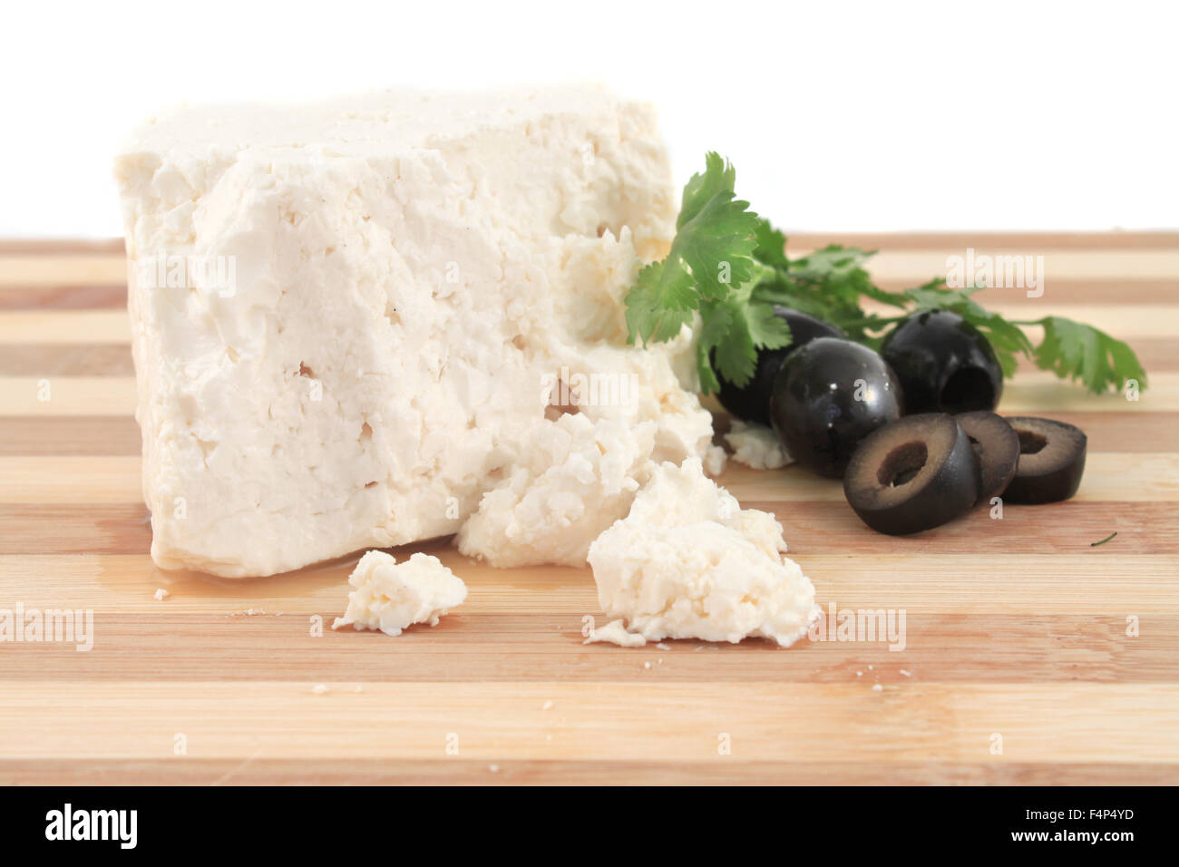 Stück Feta-Käse mit Streusel auf einem Holzbrett mit schwarzen Oliven und Koriander Stockfoto