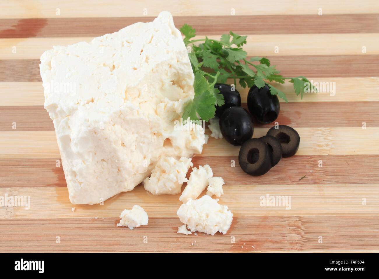 Stück Feta-Käse mit Streusel und schwarzen Oliven und Koriander auf einem Holzbrett Stockfoto