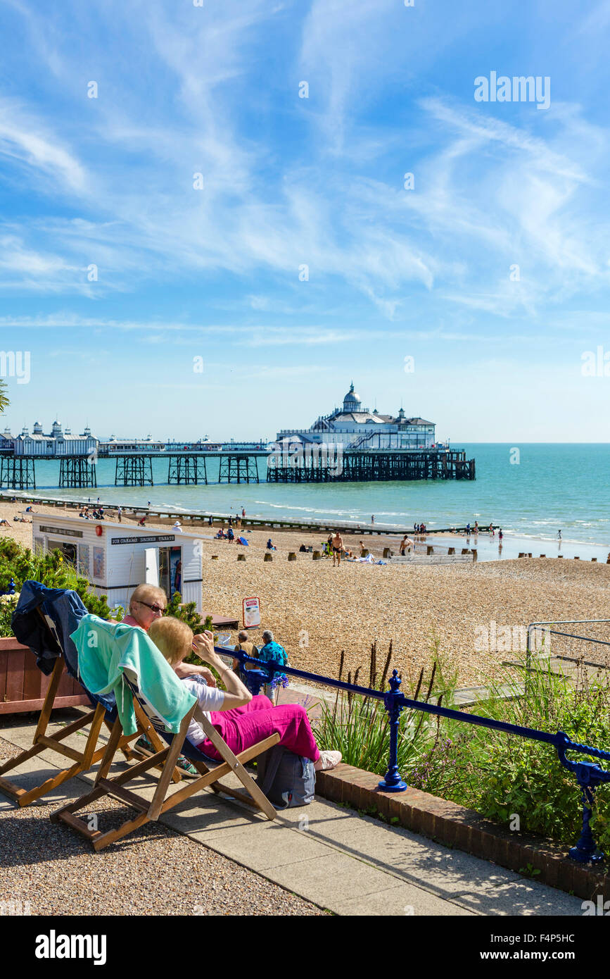 Zwei ältere Frauen sitzen auf der Promenade mit Strand und Pier hinter Grand Parade, Eastbourne, East Sussex, England, UK Stockfoto