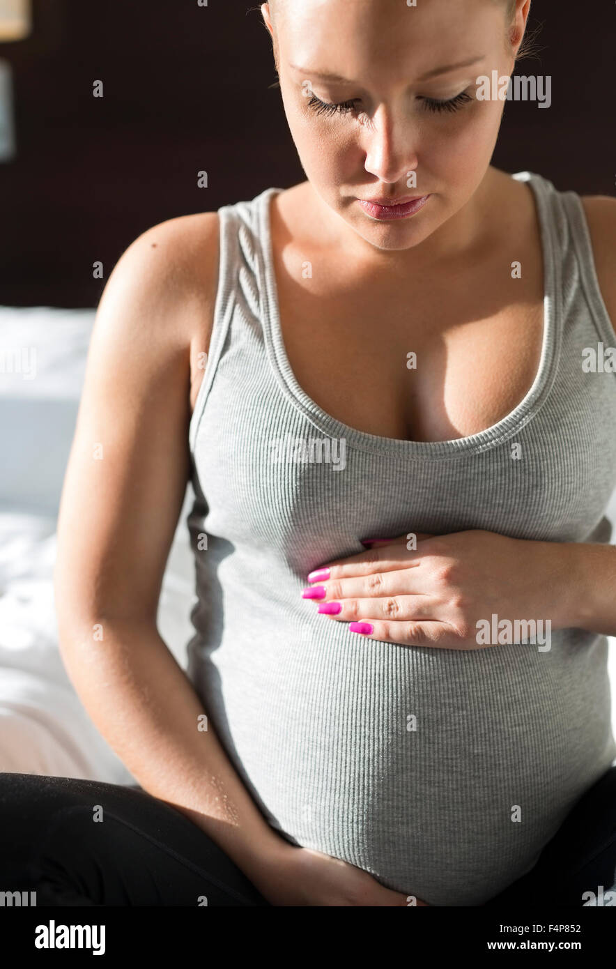 Schwangere Frau sitzt auf Bett mit der Hand am Bauch Stockfoto