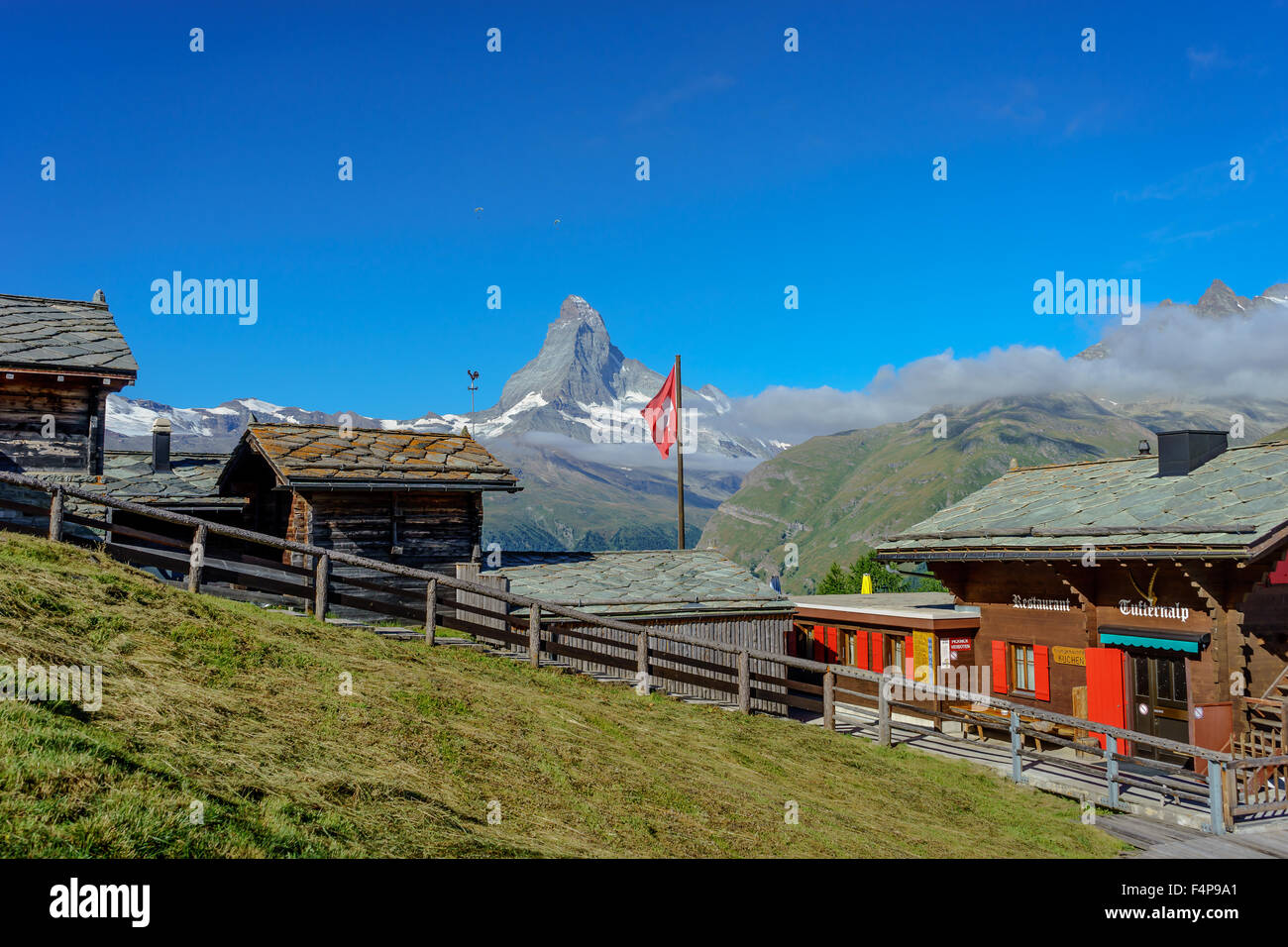 Ein Bergdorf sitzt unter Matterhorn Gipfel mit einer winkenden Schweizer Fahne. Juli 2015. Matterhorn, Schweiz. Stockfoto