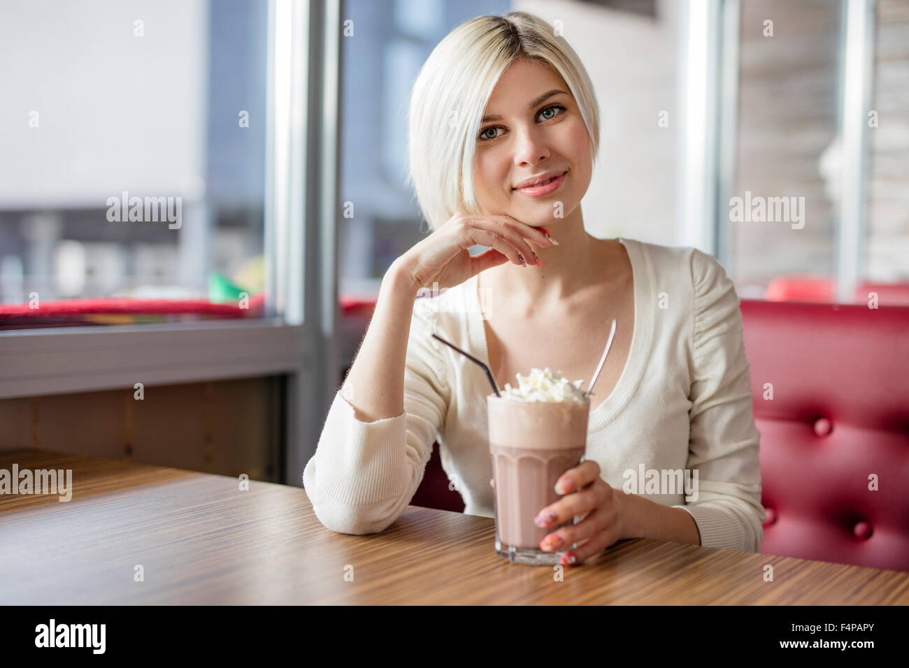 Lächelnde junge Frau trinken heißen Schokolade mit Sahne im café Stockfoto