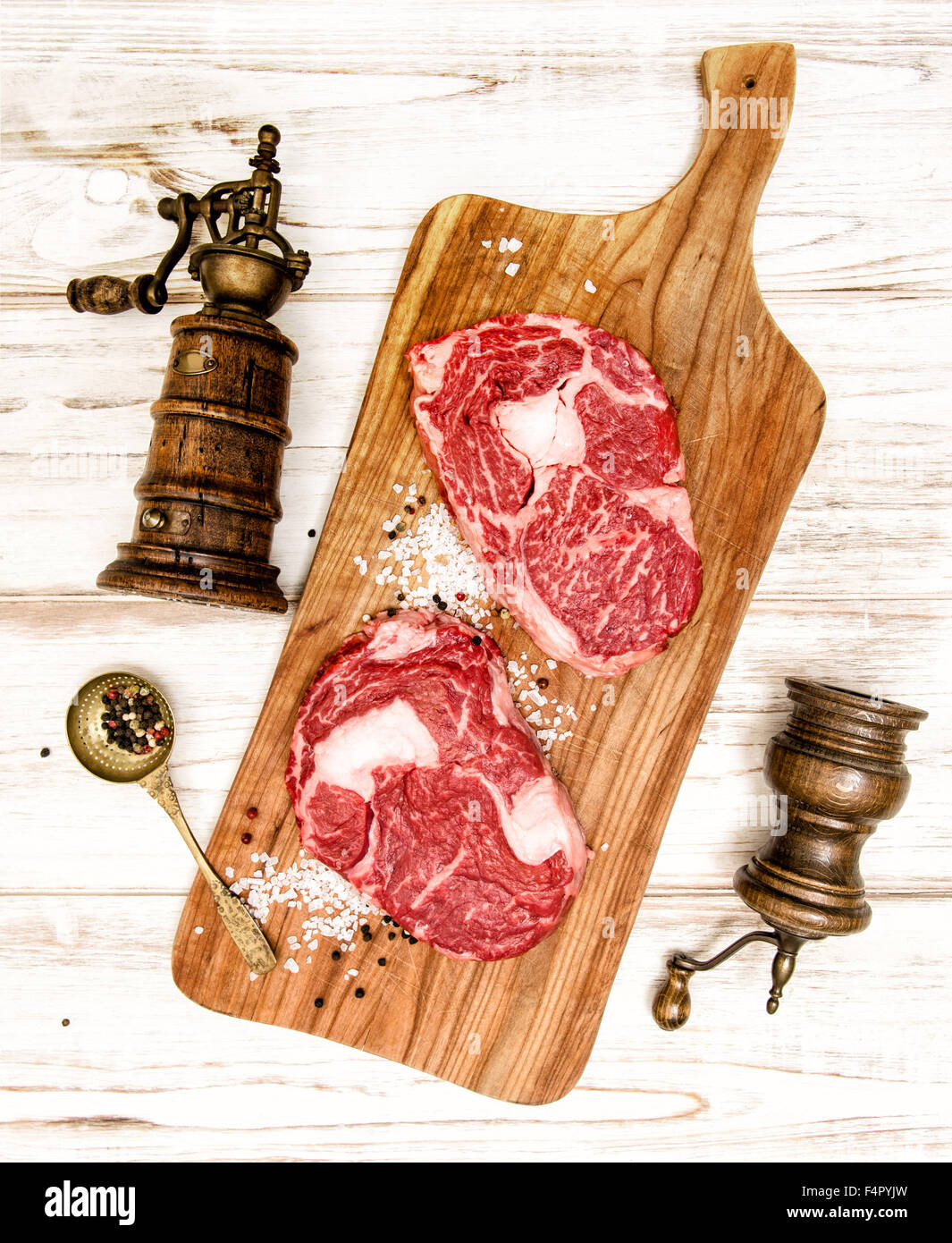 Rohes Frischfleisch Ribeye Steak mit Küchenutensilien auf Schreibtisch aus Holz. Gabel und Messer zur Zubereitung von Speisen Stockfoto