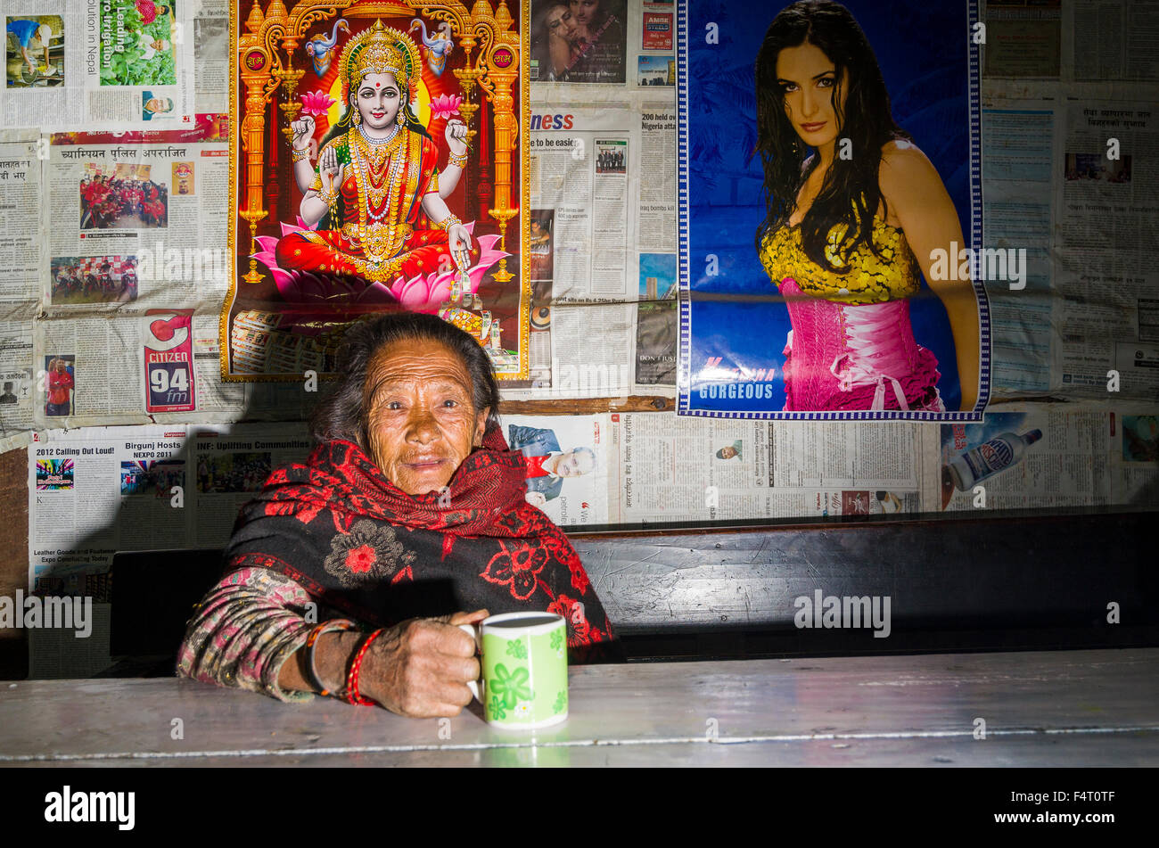 Alte Frau trinkt Tee in einem lokalen Restaurant, einige Poster an der Wand hinter Stockfoto