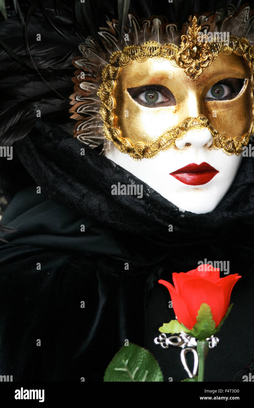 Maske der Liebe: eindringliche Frau mit erstaunlichen Augen im goldenen weichkantige Maske mit schwarzer Spitze Kleidung und rote Rose am Karneval in Venedig Stockfoto