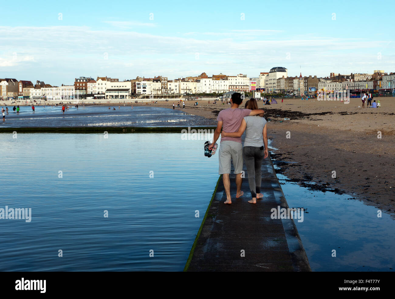 A junges Paar, mit ihre Arme umeinander, Spaziergang entlang der Mauer auf den Gezeiten Baden Pool, am Strand von Margate, Kent. Stockfoto