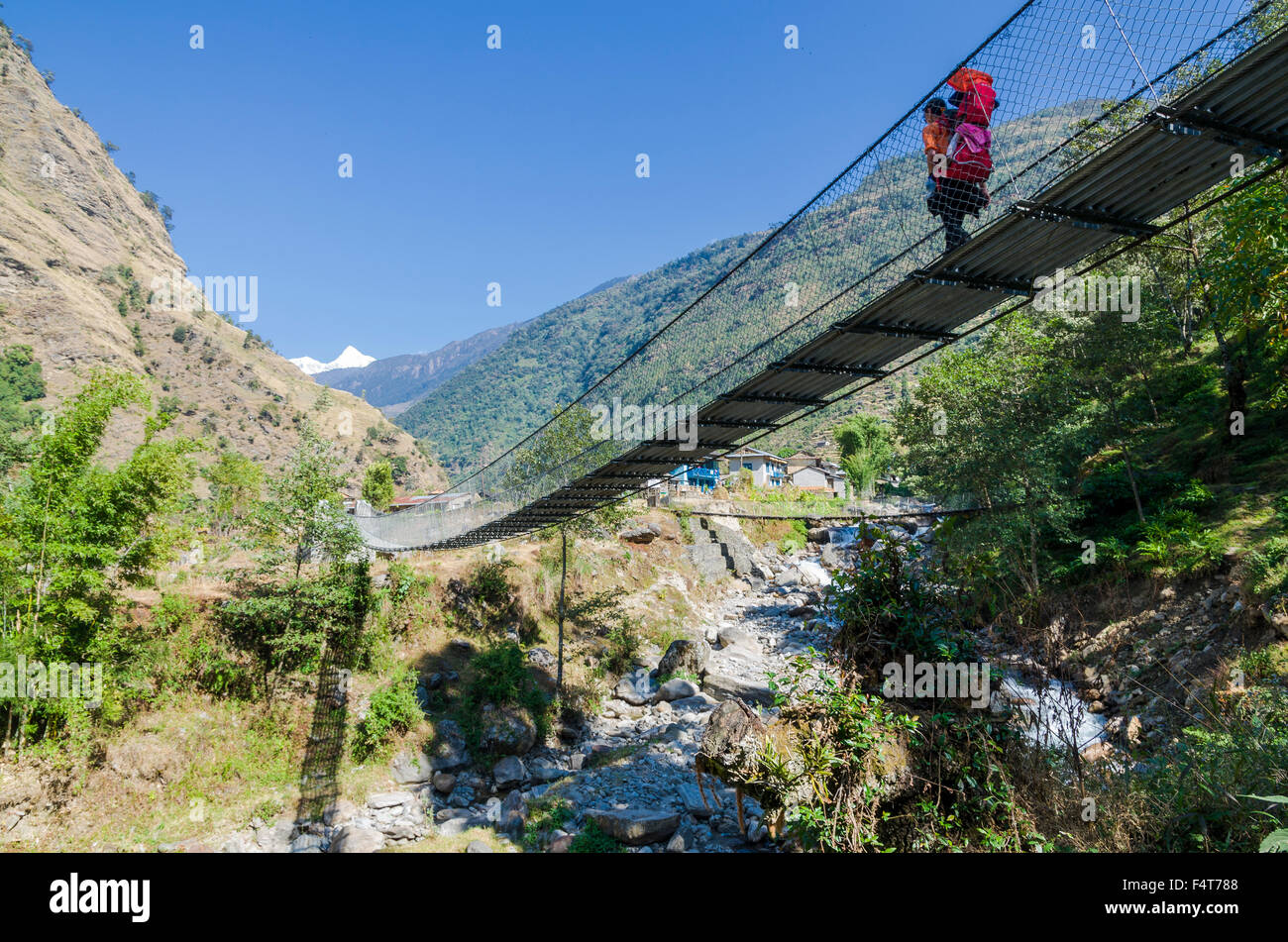 Junge touristische Frau, die ihr Kind in einem Rack auf dem Rücken tragen, überqueren eine Hängebrücke Stockfoto