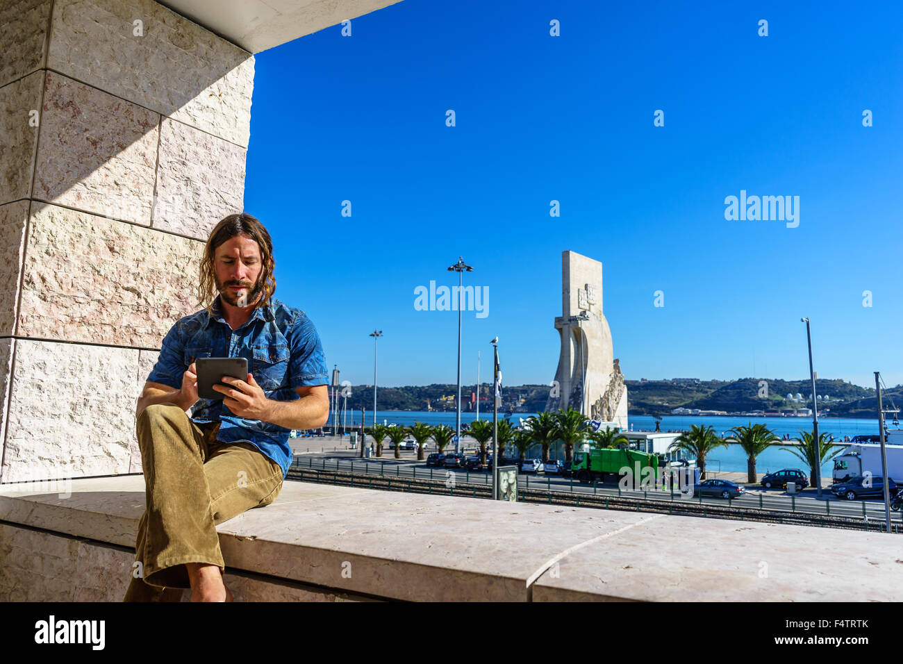 Man liest aus einem elektronischen Tablet vor der portugiesischen Ikone, Denkmal der Entdeckungen Padrão Dos Descobrimentos. Stockfoto