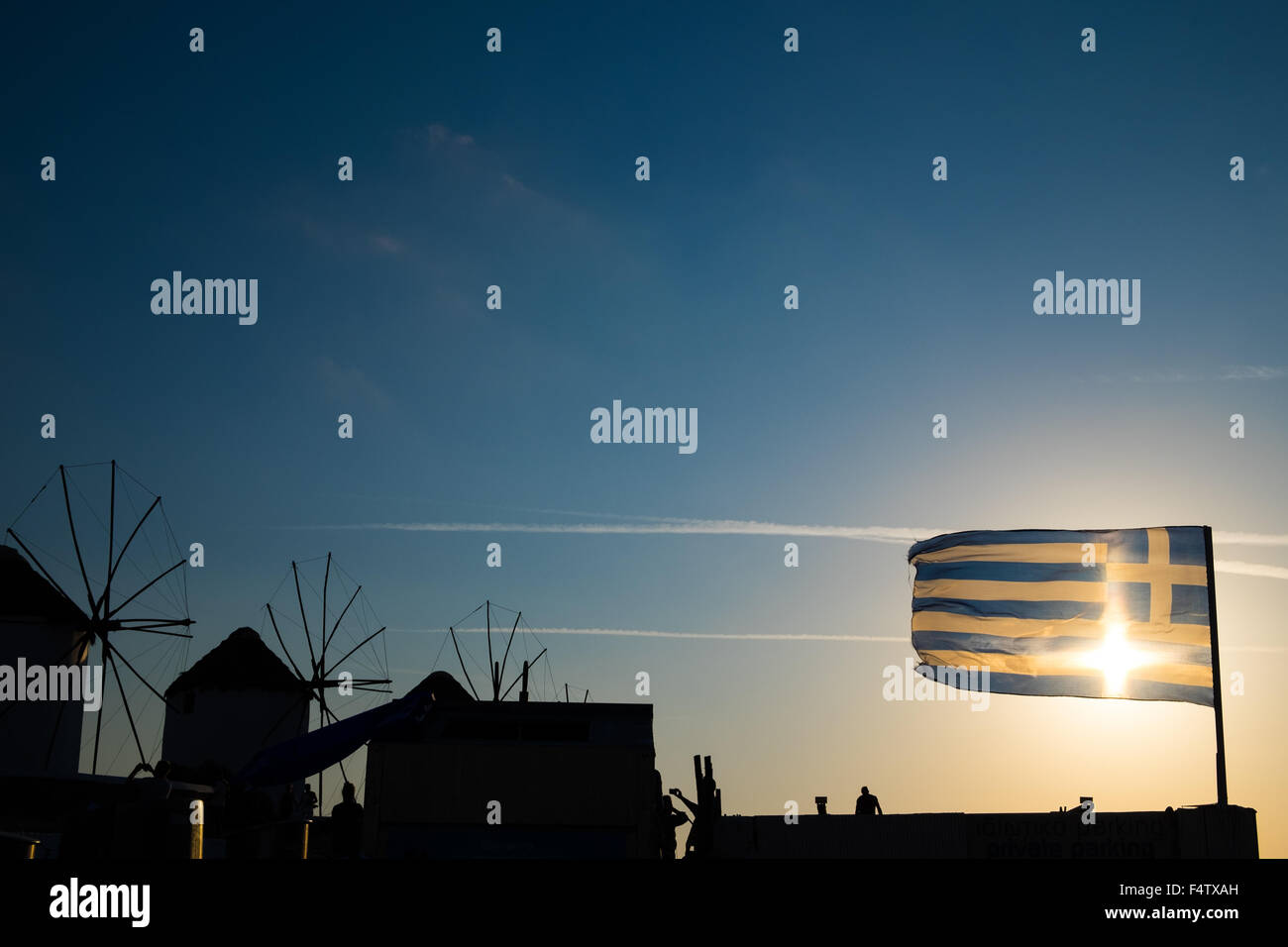 Mykonos Windmühlen bei Sonnenuntergang mit griechischer Flagge im Vordergrund. Stockfoto