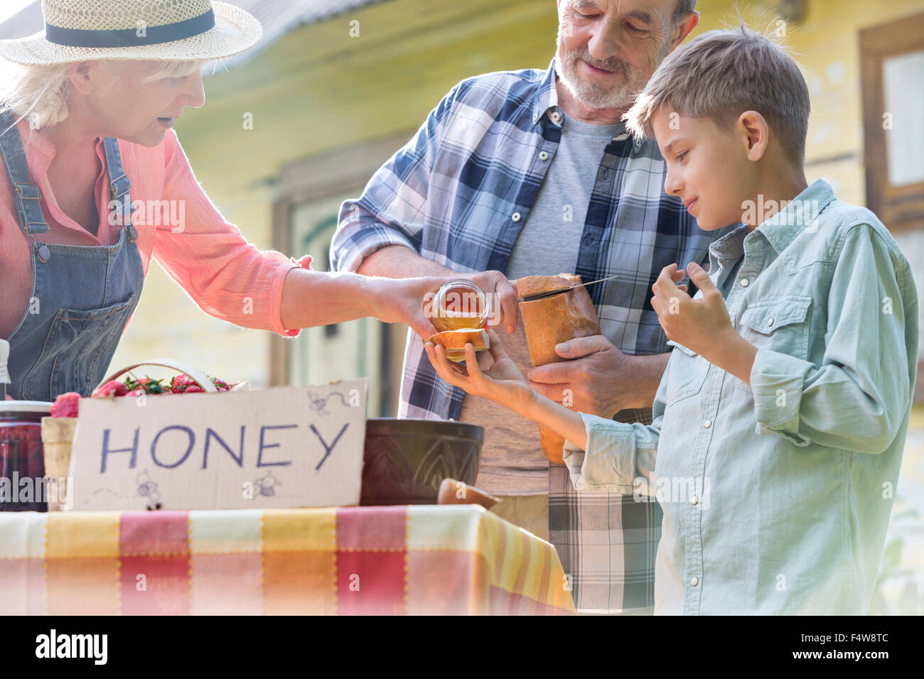 Großeltern und Enkel, Verkostung und Verkauf von Honig an Bauern Marktstand Stockfoto