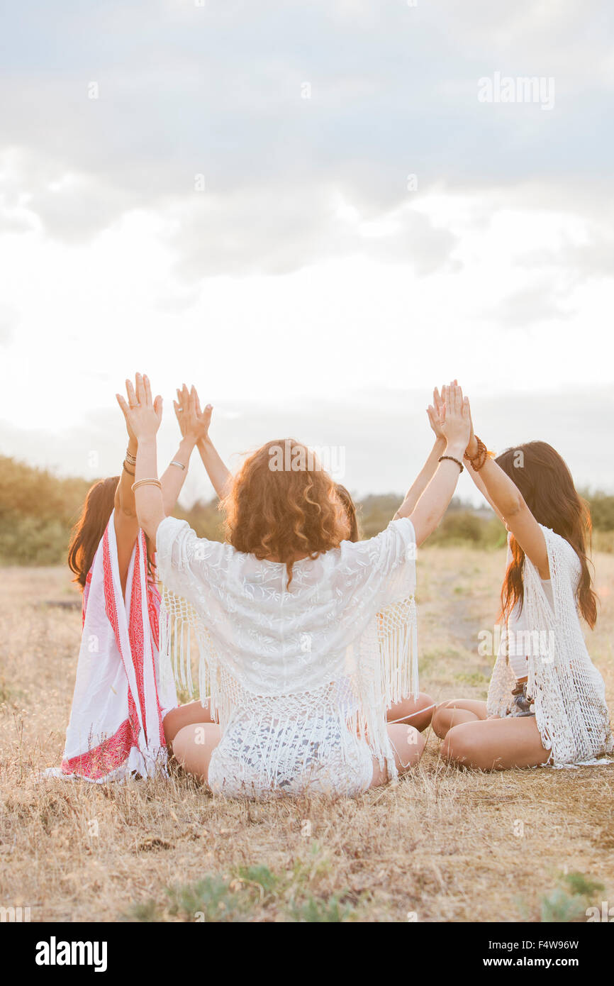 Boho Frauen sitzen im Kreis mit Armen angehoben und im ländlichen Bereich verbunden Stockfoto