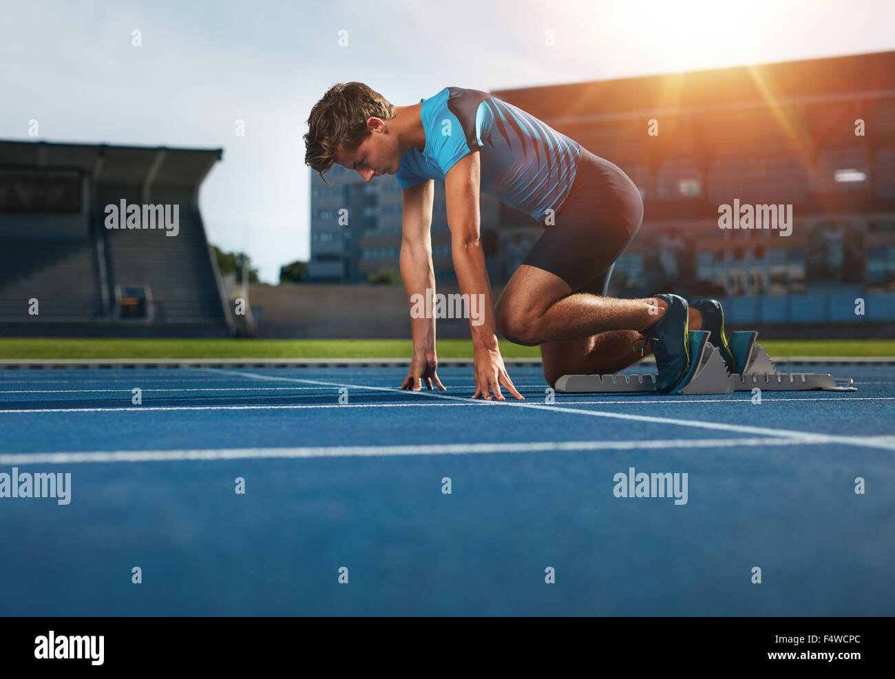 Junge Sportler in Ausgangsposition bereit, ein Rennen zu starten. Männliche Läufer bereit für sportliche Übung auf Rennstrecke mit Sonne Flare. Stockfoto