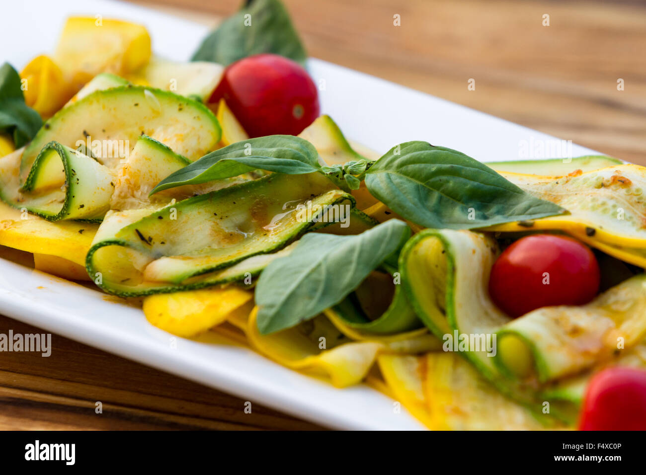 frische Zucchini gebraten mit frischem Basilikum und Olivenöl in einer leichten Tomatensauce serviert auf einem weißen Teller Stockfoto