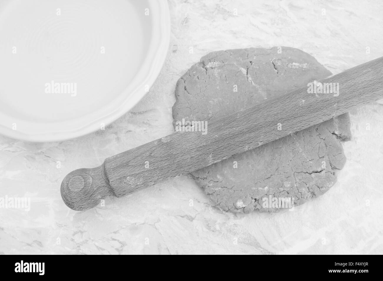 Roll-out selbstgemachter Kuchen mit einem hölzernen Nudelholz neben Keramik Kuchenform - monochrome Verarbeitung Stockfoto