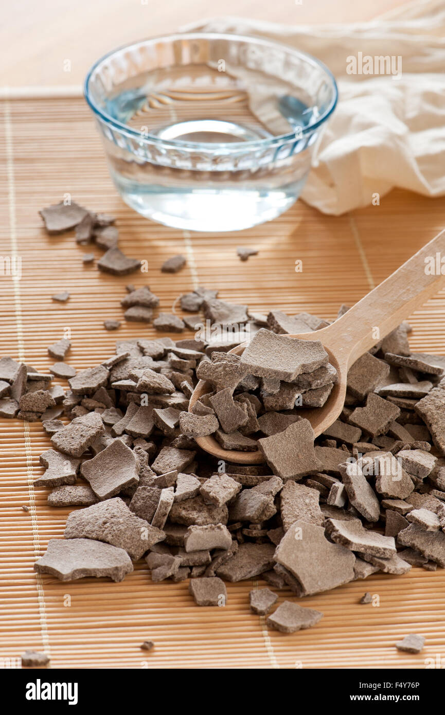 Ghassoul Lava Ton häufen, getrockneten Späne verschüttet Out, Glasschale mit Wasser und Holzlöffel auf Matte, zerbröckelte marokkanischen Rhassoul... Stockfoto