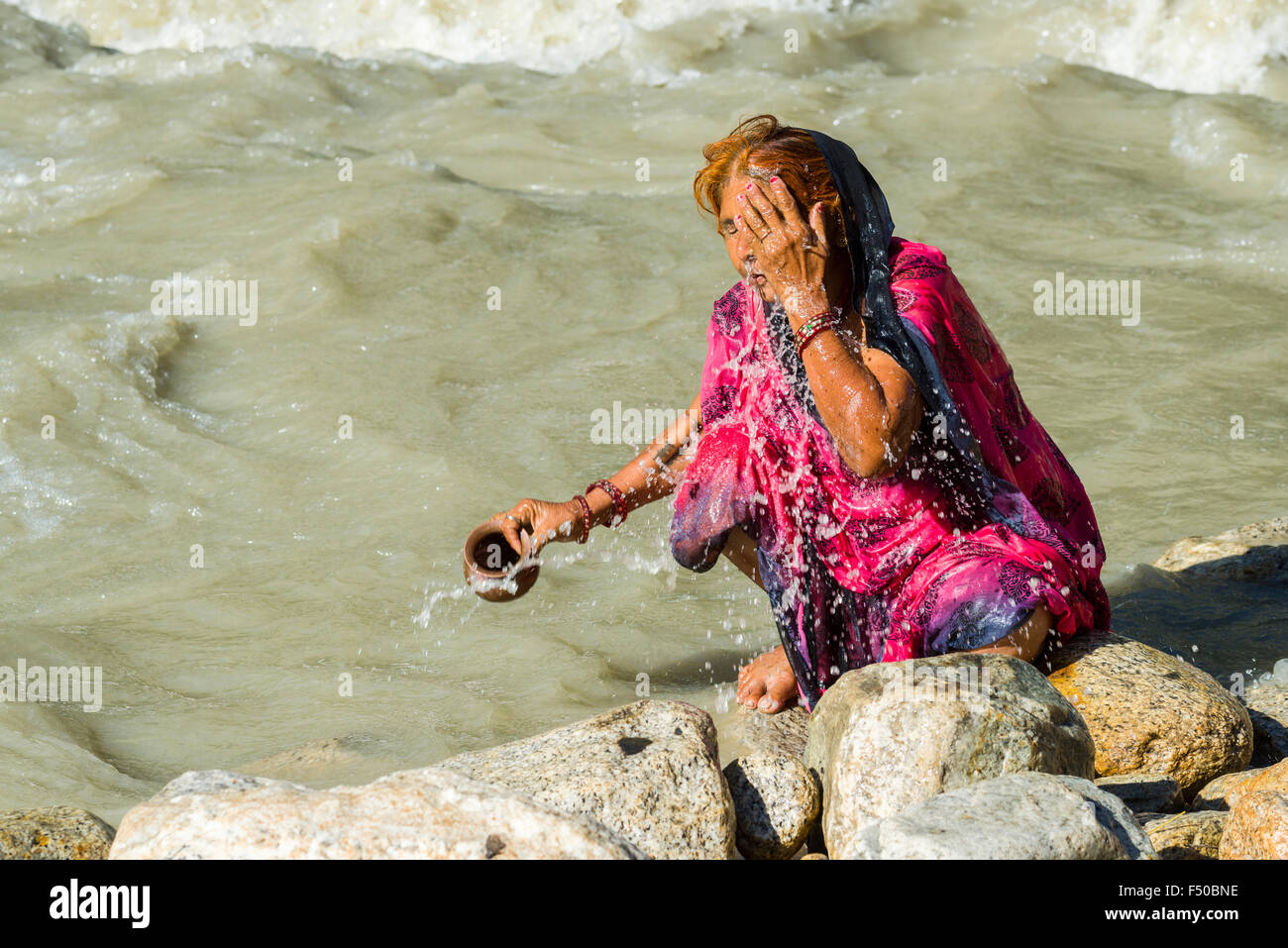 Ein weiblicher Pilger an den Ufern des Flusses Ganges ist unter der Dusche mit dem heiligen Wasser Stockfoto