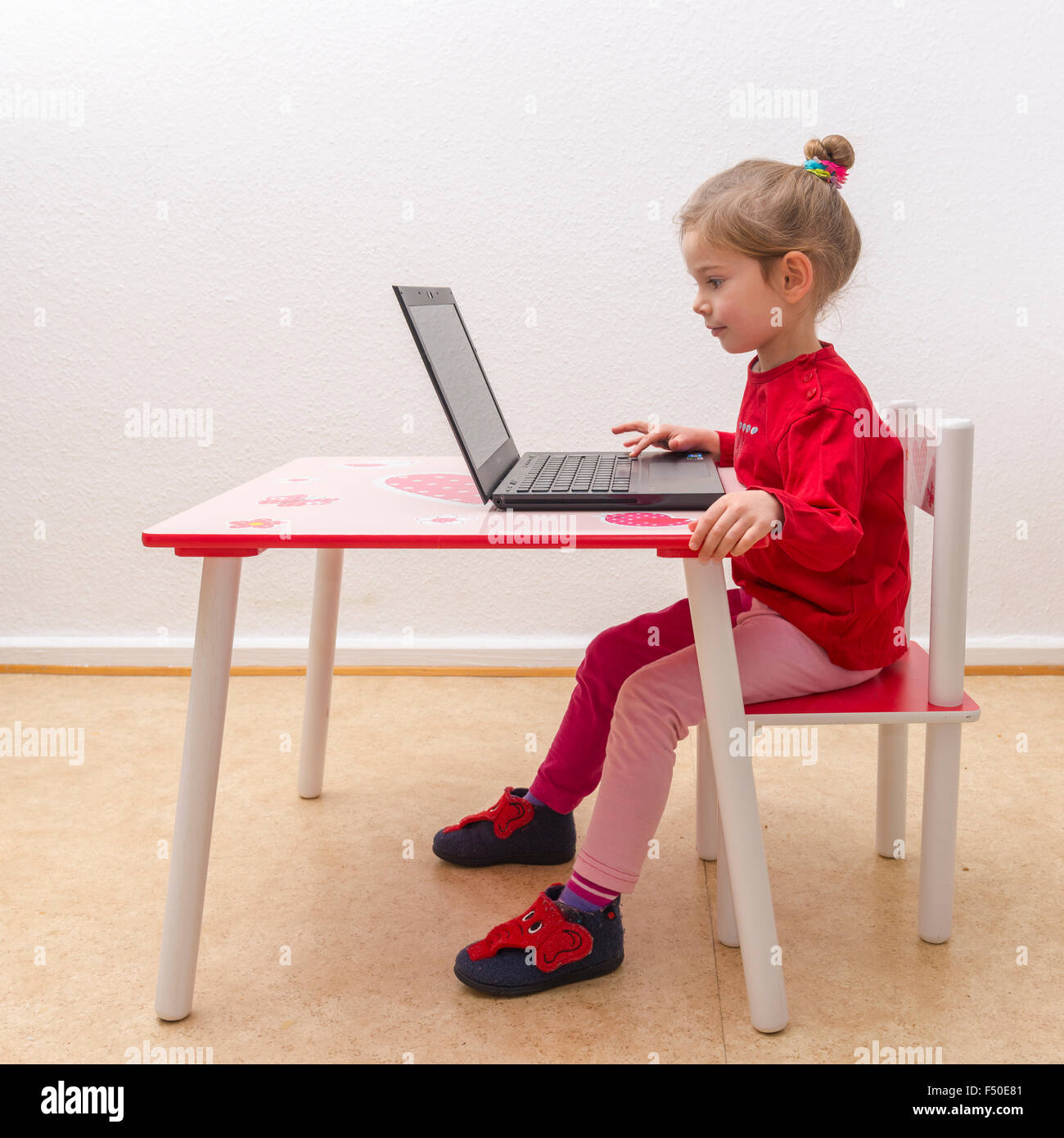 Eine blonde drei Jahre altes Mädchen sitzt vor einem Notebook, Laptop, beobachten Sie den Bildschirm und mit der Tastatur Stockfoto