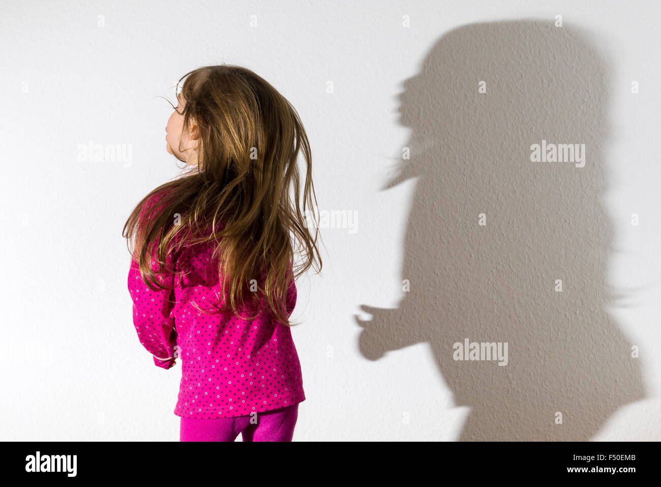 Eine blonde drei Jahre altes Mädchen, trägt ein rosafarbenes Hemd, Tanzen ist vor einer weißen Wand, ihr Schatten hinter ihr verlassen Stockfoto