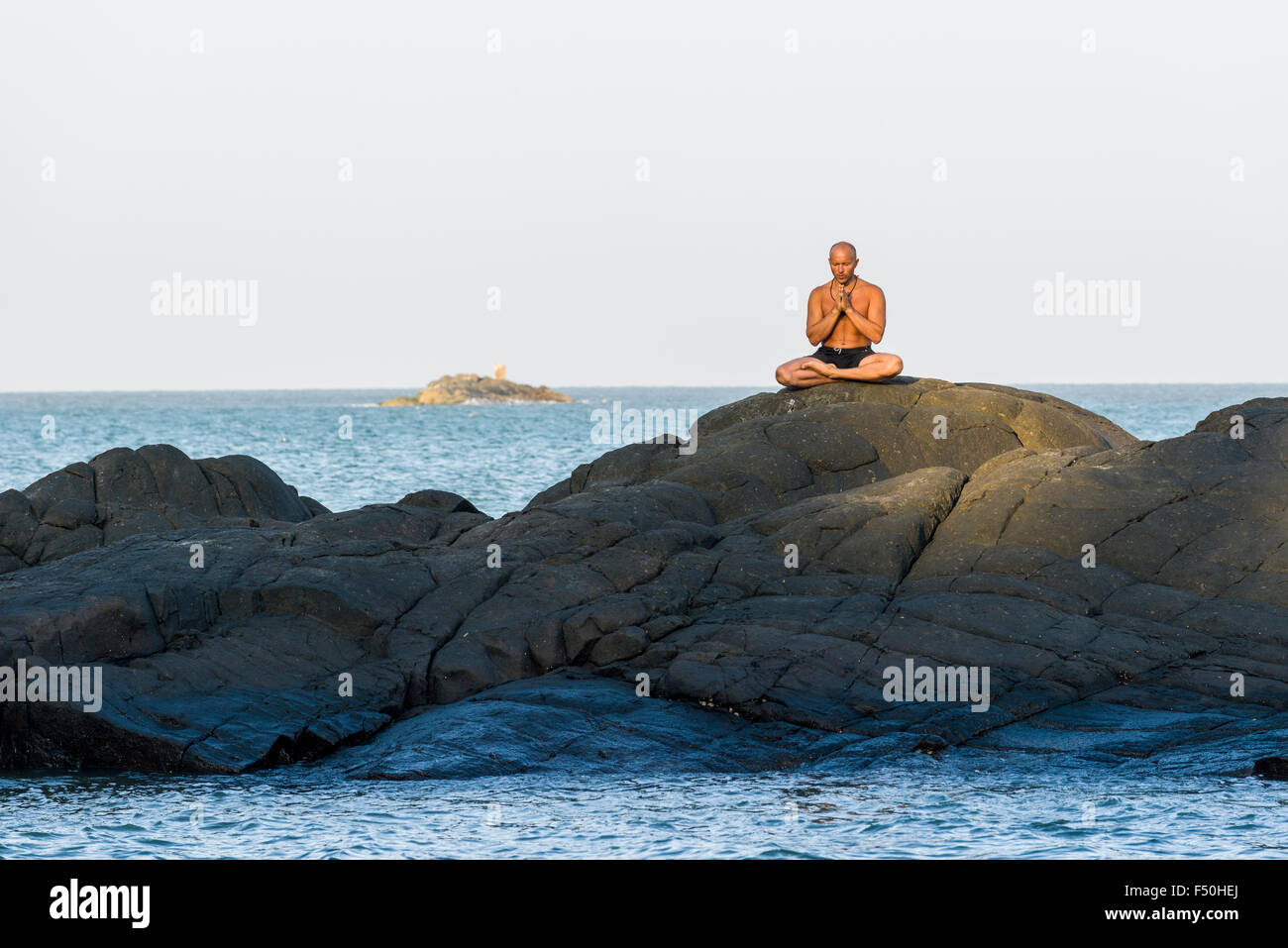 Ein Mann ist zu meditieren, Yoga auf einem Felsen am kudle Strand, einem der berühmten Strände neben dem Tempel der Stadt und der Wallfahrt Stockfoto