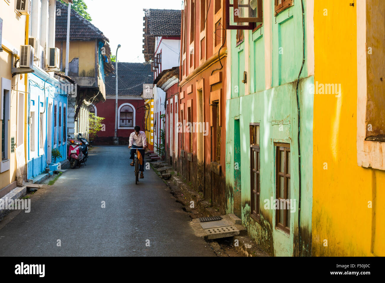 Eine kleine Gasse mit bunten Häusern und ein Radfahrer in der Hauptstadt von Goa, ehemalige portugiesische Kolonie Stockfoto