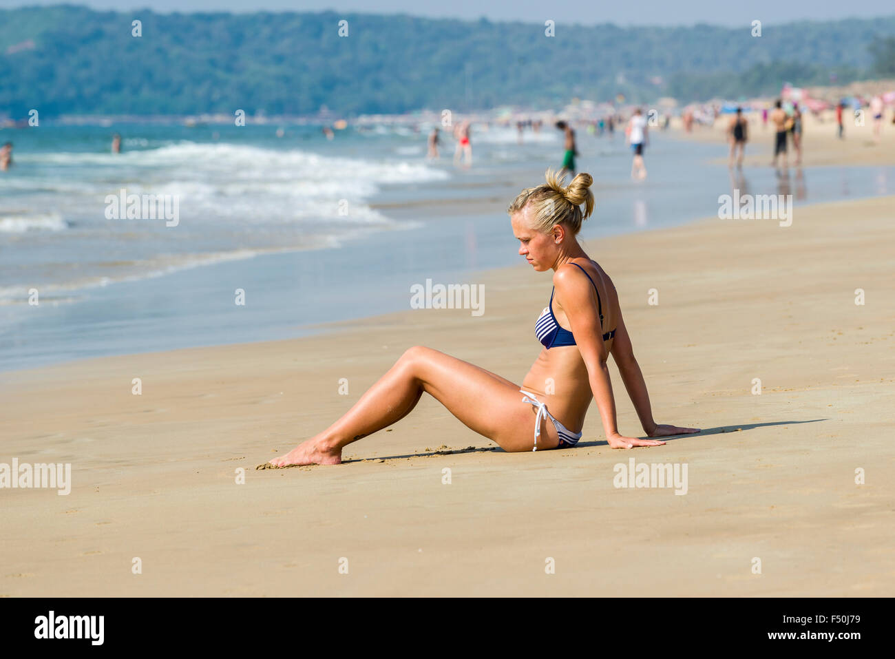 Eine junge Frau mit blondem Haar, tragen, Bikini, sitzt im Sand von Calangute Beach in der ehemaligen portugiesischen Kolonie Goa Stockfoto