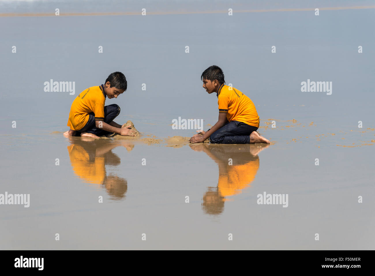 Zwei Schüler, tragen gelbe Hemden, Spielen mit Sand am Strand, die Spiegelung im Wasser Stockfoto