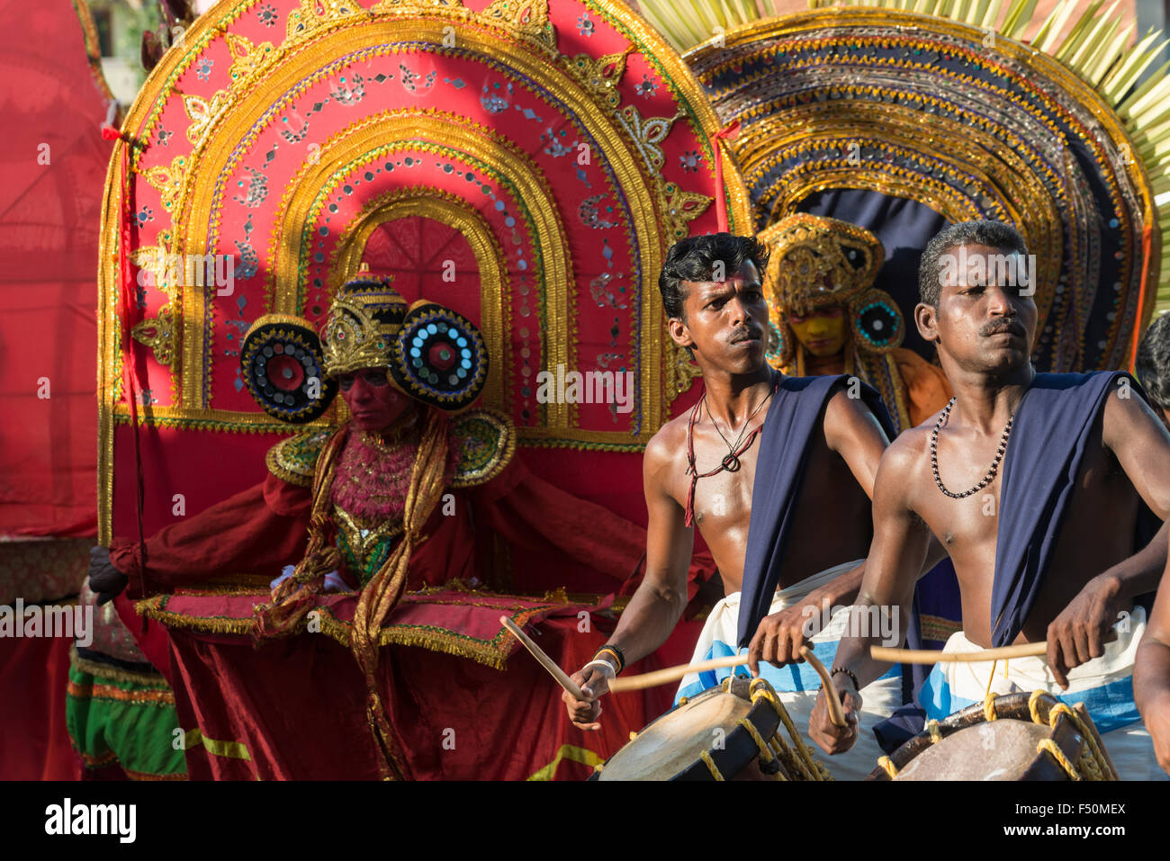 Zwei Schlagzeugern spielen ihre Instrumente an einem Tempel Festival, theyyam Tänzer mit gelben und roten Kostüme hinter Ihnen Stockfoto