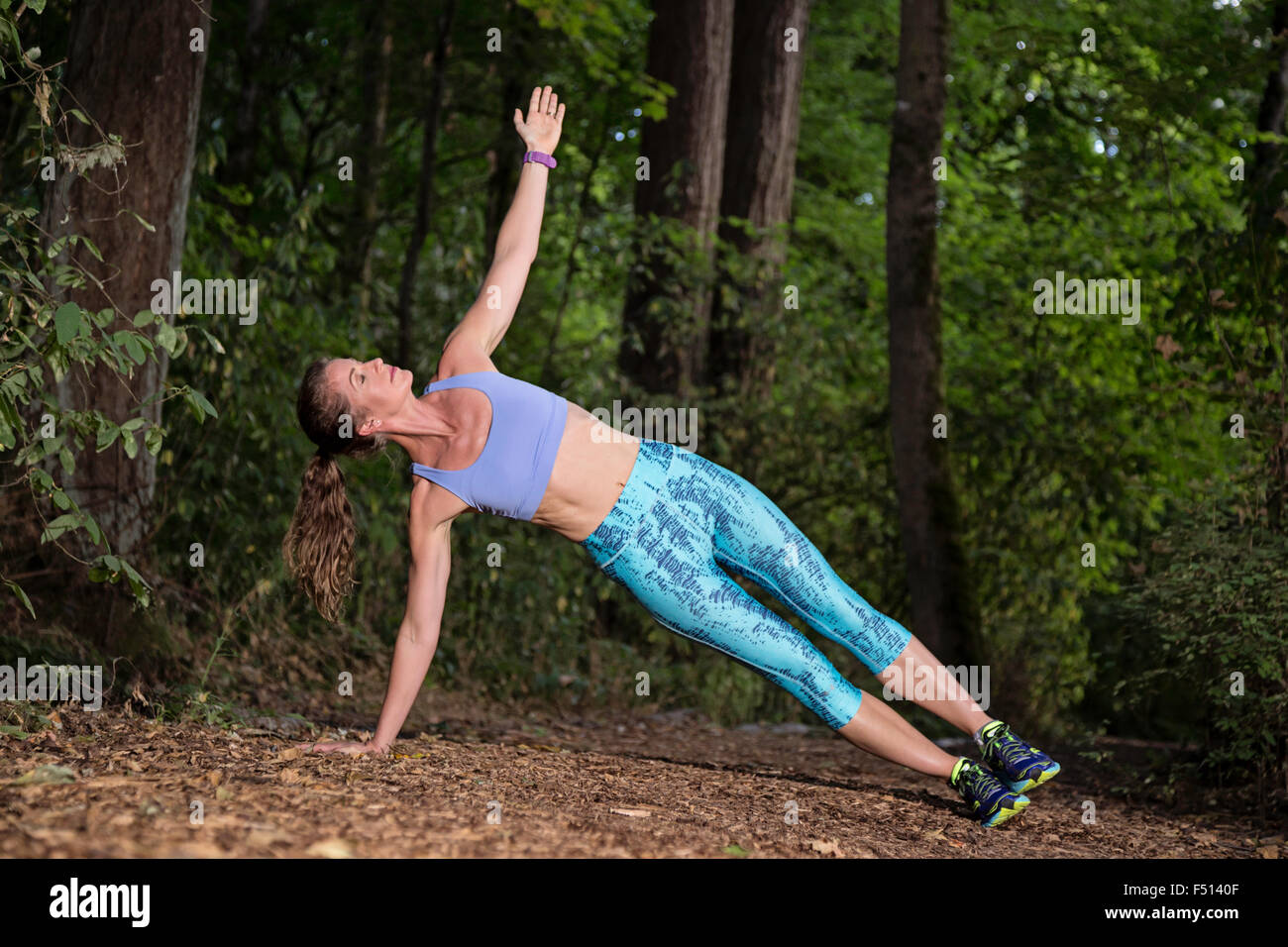 Sportliche Frau macht eine Seite Planke posieren auf einem Waldweg Stockfoto