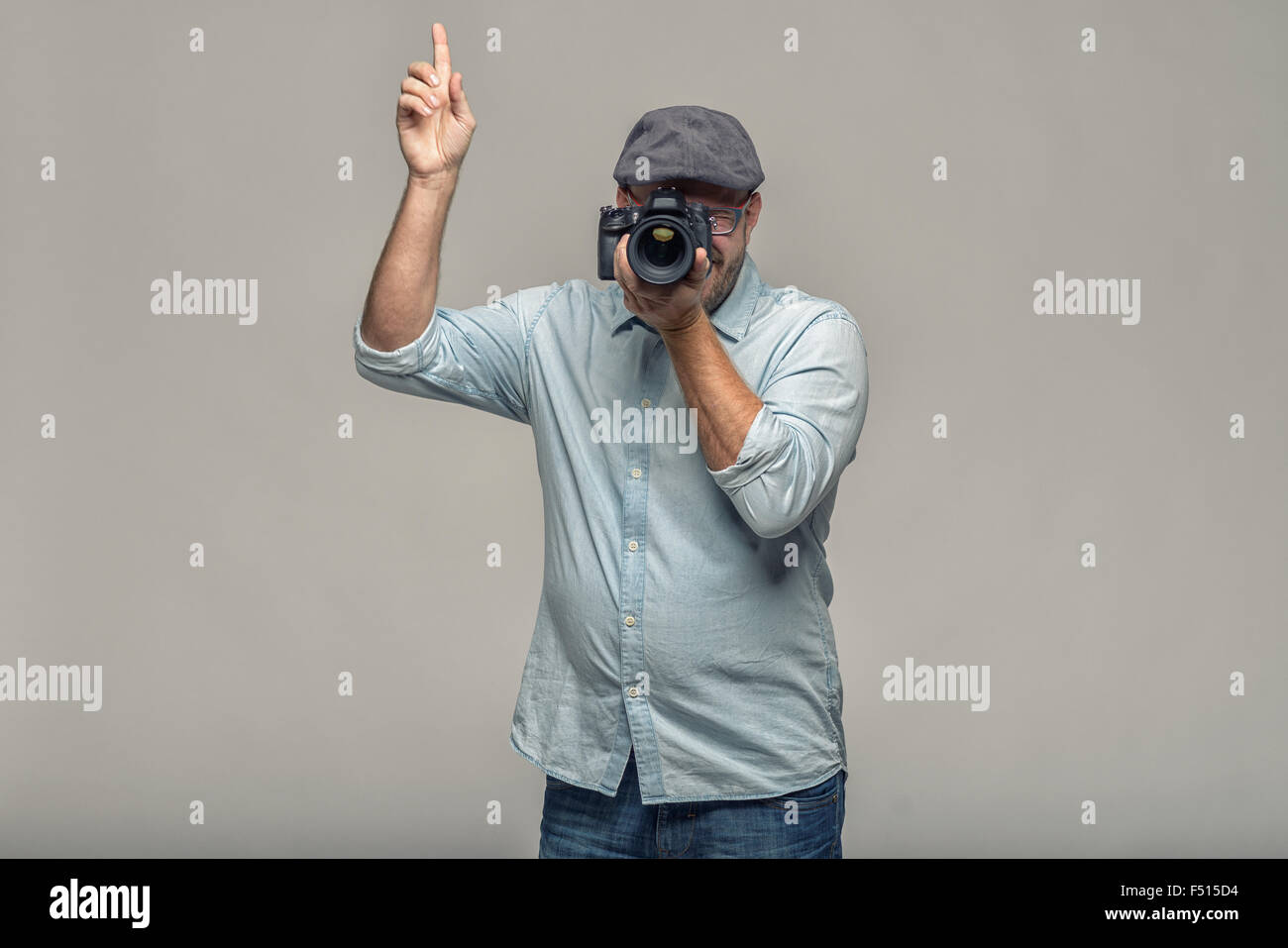 Mann in einer Kappe hält seine Kamera auf sein Auge mit einer Hand komponieren ein Foto nach oben zeigend mit seiner anderen Hand geben inst Stockfoto