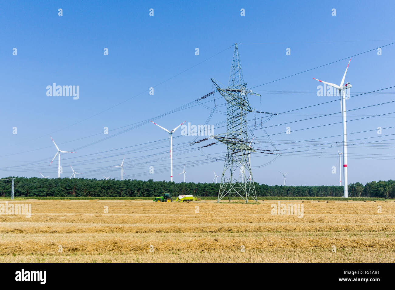 Eine Leitung ist der Kreuzung einem Abgeernteten Feld, ein Traktor und etwas Wind Triebwerke in der Ferne Stockfoto