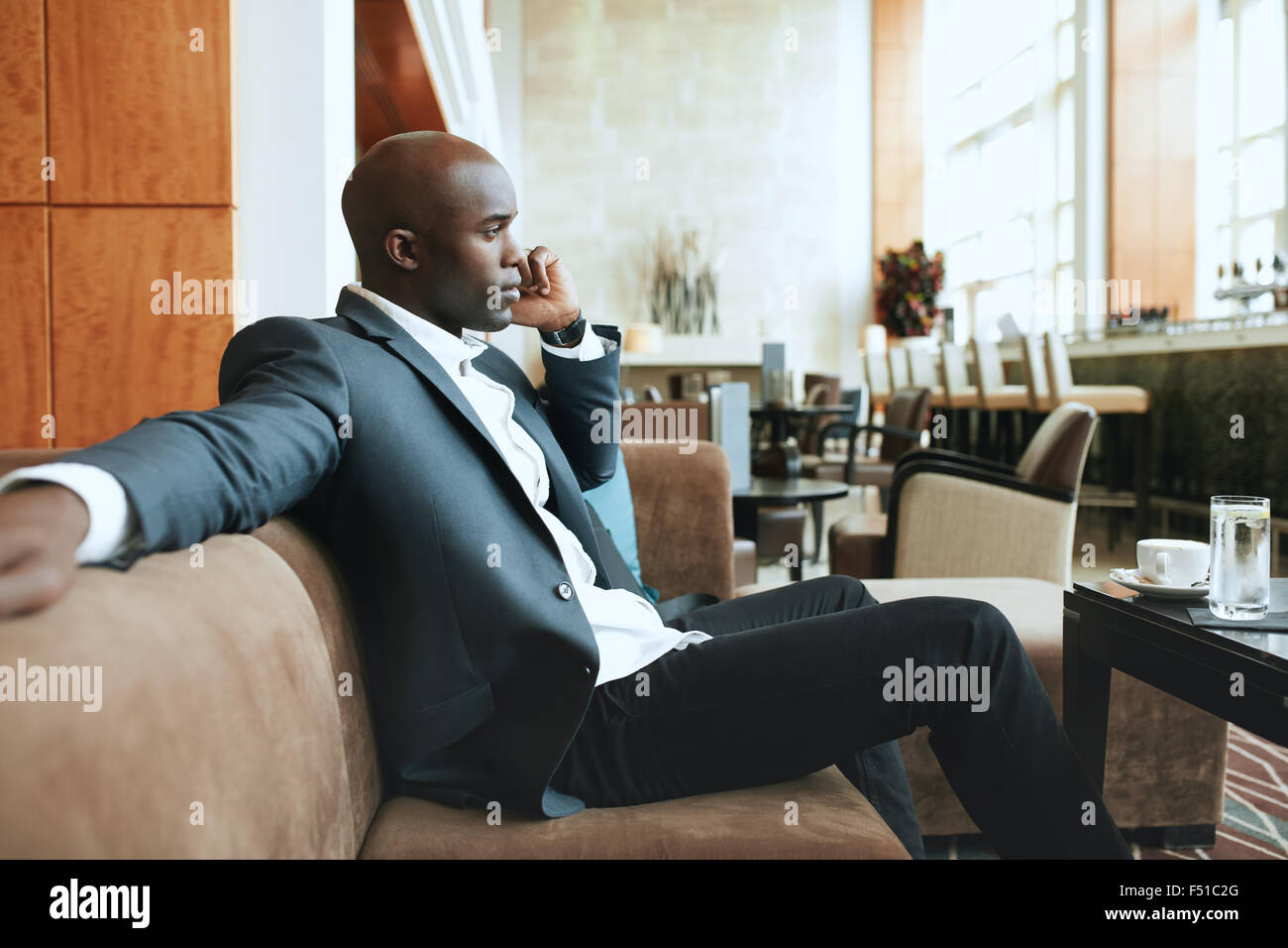 Junger Geschäftsmann sitzt entspannt auf Sofa in der Hotellobby einen Anruf tätigen wartet auf jemanden. Stockfoto