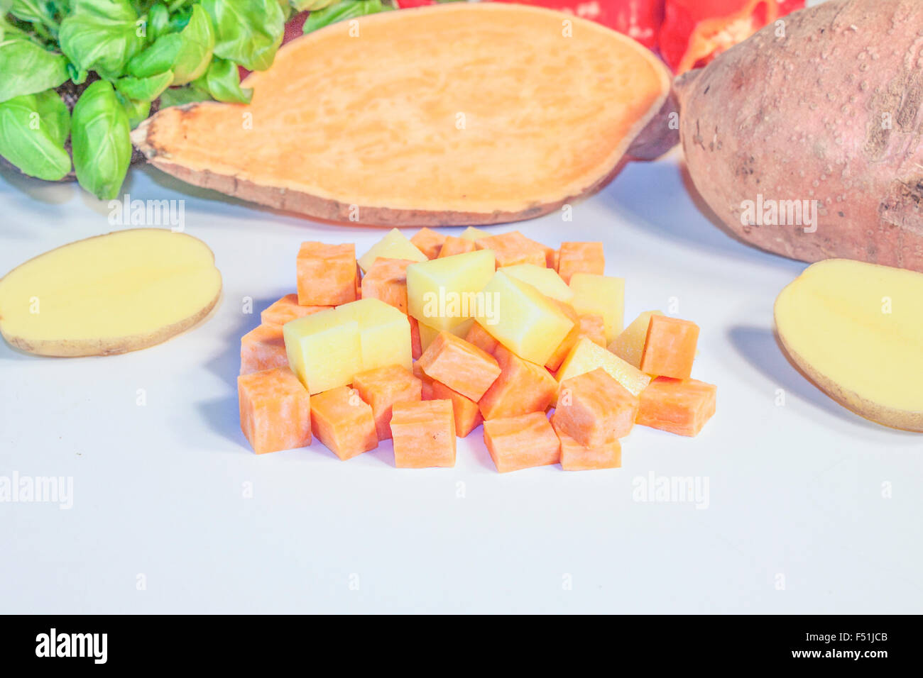 Süßkartoffeln und Kartoffeln in Würfel schneiden, vor Kräuter und Gemüse Stockfoto