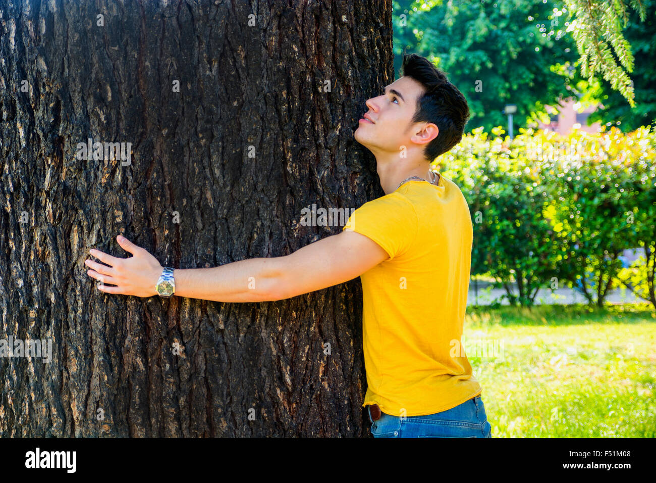 Lächelnd hübschen jungen Mann umarmt einen Baum nach oben, im Stadtpark Stockfoto