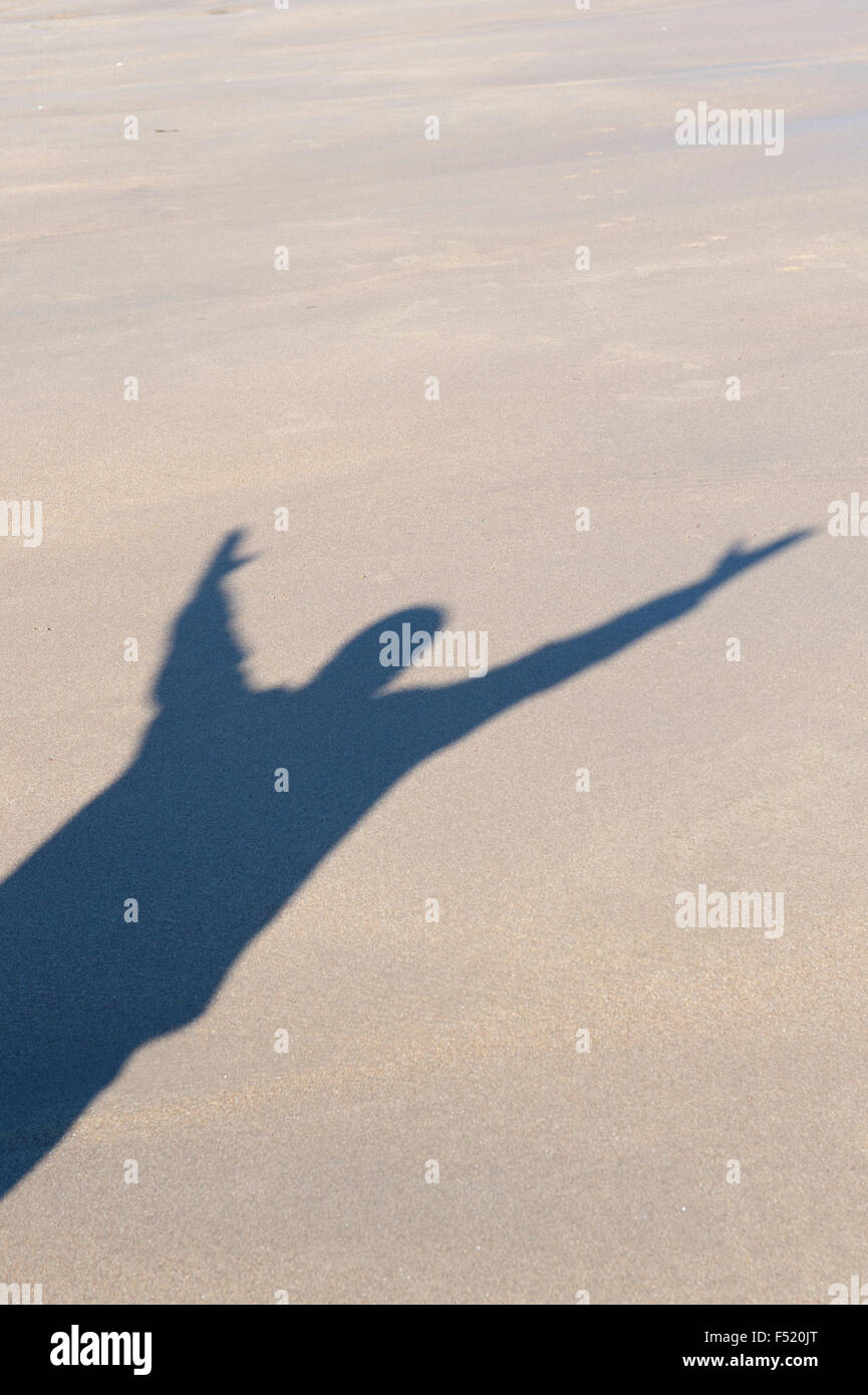 Schatten eines Mannes mit seinen Armen in der Luft am Strand. UK Stockfoto