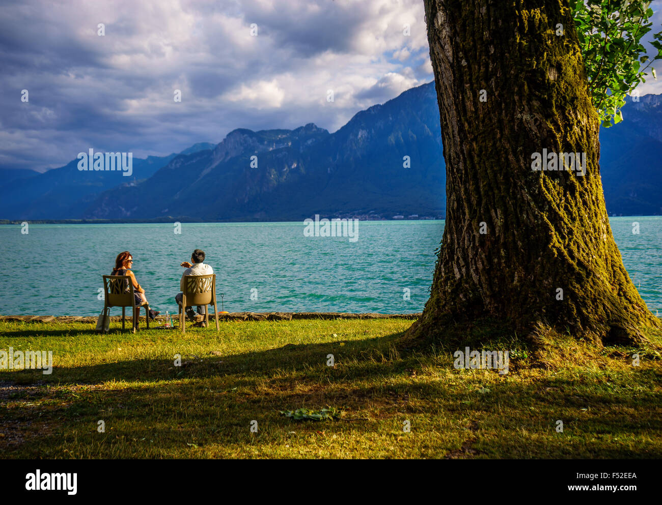 Ein paar entspannt am Genfer See im Sommer neben einem großen Baum. Genfer See, Schweiz. Stockfoto