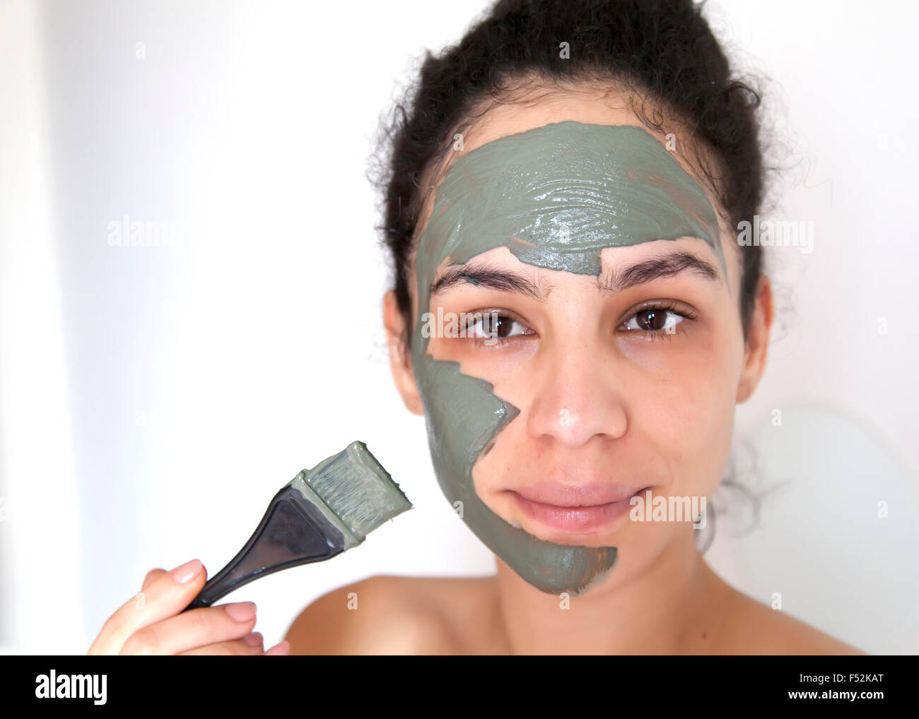Schöne junge brasilianische Modell mit grüner Tonerde Gesichtsmaske. Spa-Teenager-Mädchen Gesicht Gesichtsmaske anwenden. Beauty-Behandlungen. Stockfoto
